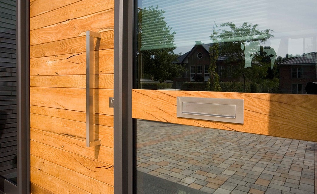 Eine Holzhaustür. Direkt daneben eine Glasfront mit eingebauter Holzblende und Briefkastenschlitz.