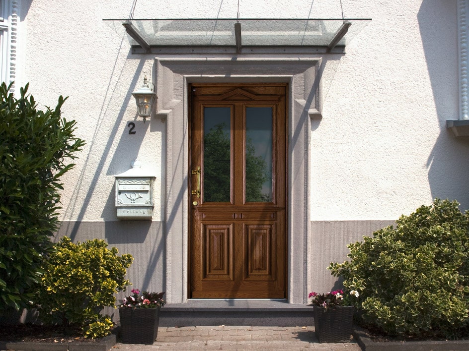 Eingangsbereich eines weißen Wohngebäudes mit einer Holzhaustür.