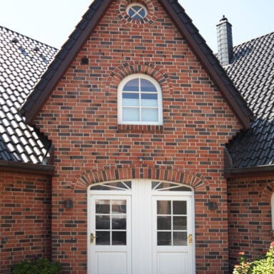 Wohnhaus mit Haustüren und abgerundetem Fenster darüber.